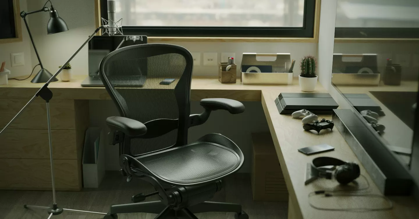 Home office with a mesh task chair, oak desk, studio microphone on a boom stand and a window behind